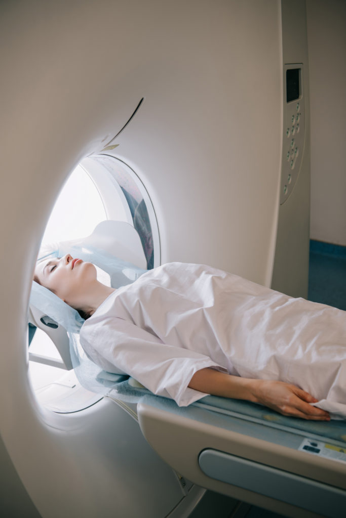 woman with closed eyes lying on computed tomography scanner table during radiology test