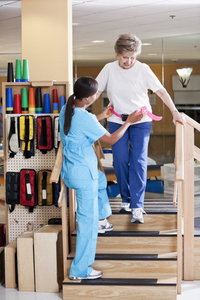 African American physical therapist (40s) working with senior patient (80s) walking down stairs. The senior is undergoing occupational therapy