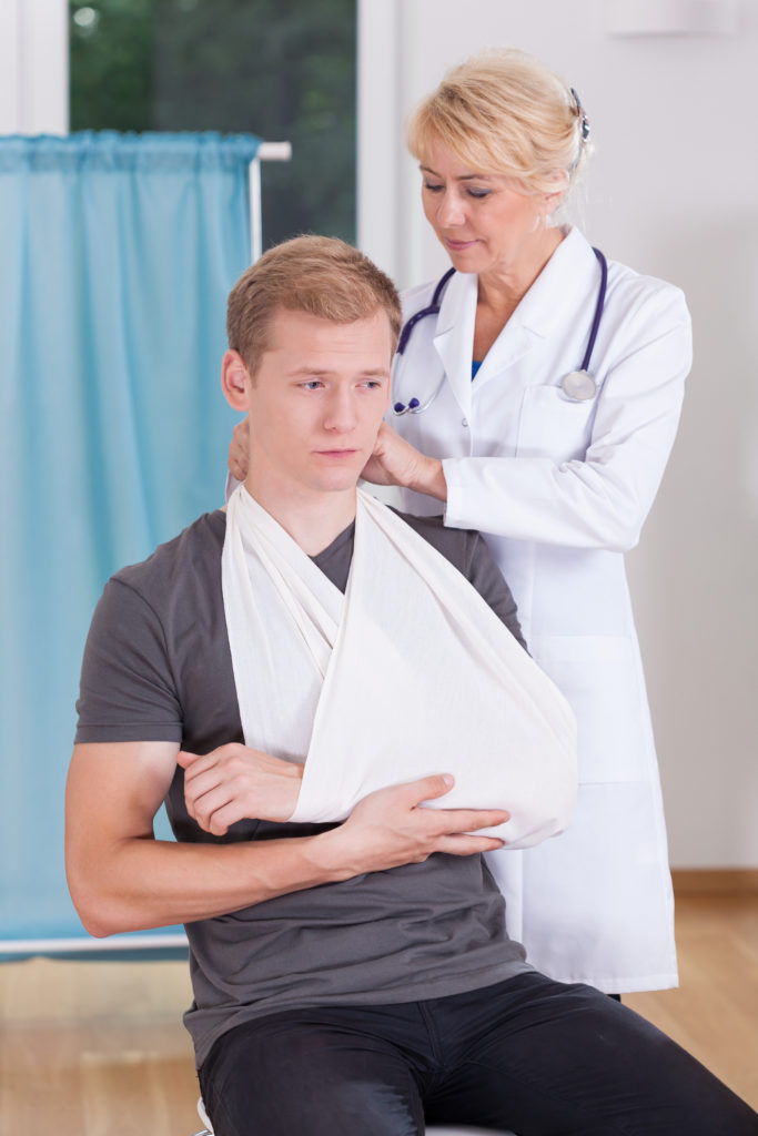 Patient wearing an elbow sling after undergoing Brachial Plexus Palsy surgery. A doctor is standing behind the patient helping him put the sling on