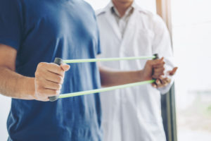 Physiotherapist man giving resistance band exercise treatment About Chest muscles and Shoulder of athlete male patient Physical therapy concept