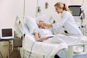 DO not worry. Friendly female medical worker smiling while helping her retired patient and adjusting an oxygen mask at hospital.